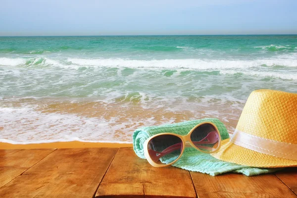 Fedora Hut und Sonnenbrille über Holztisch und Meer — Stockfoto