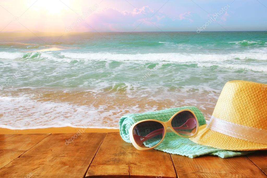 Fedora hat and sunglasses over wooden table and sea ⬇ Stock Photo