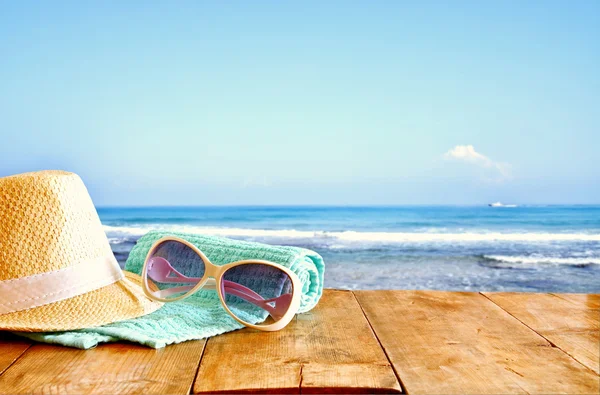 Шляпа и солнцезащитные очки на деревянном столе и морском фоне — стоковое фото