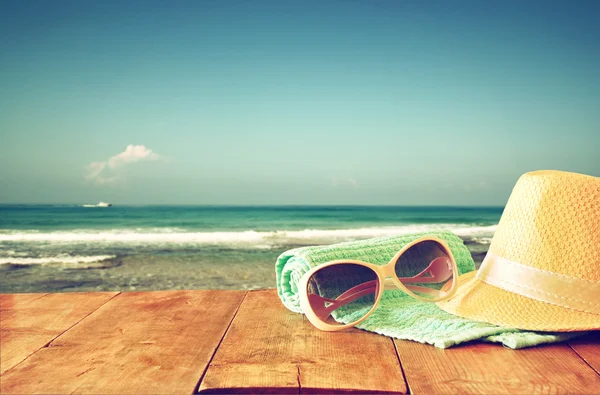 Sombrero fedora y gafas de sol sobre mesa de madera y paisaje marino —  Fotos de Stock