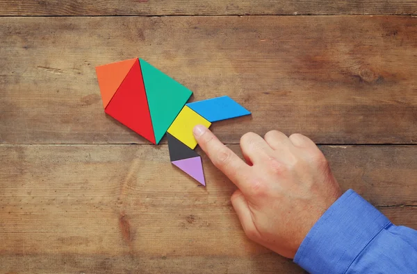 Man 's hand pointing at rocket made from square tangram puzzle — стоковое фото