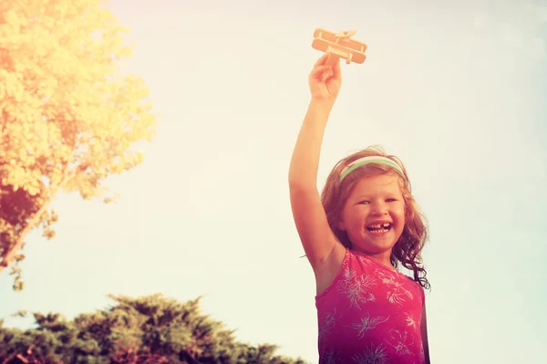 Gadis kecil yang lucu memegang mainan kayu pesawat melawan langit — Stok Foto