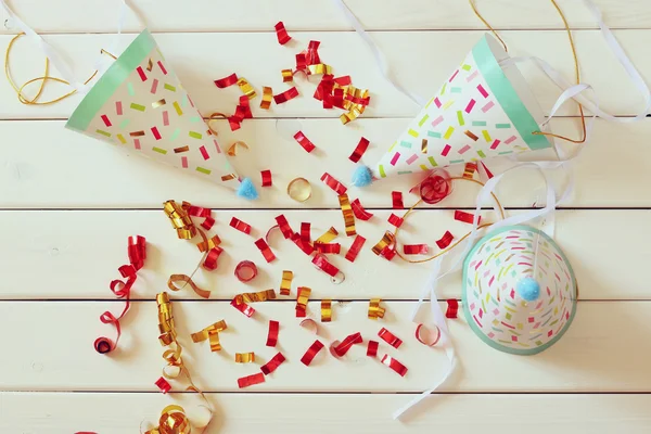 Party hat next to colorful confetti on wooden table