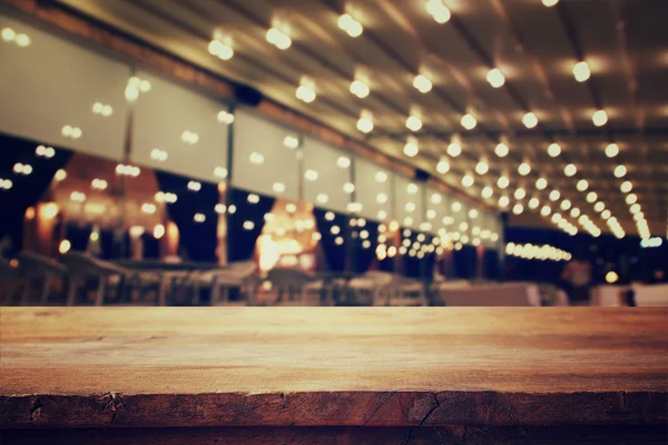 Wooden table in front of abstract blurred restaurant lights — Stock Photo, Image