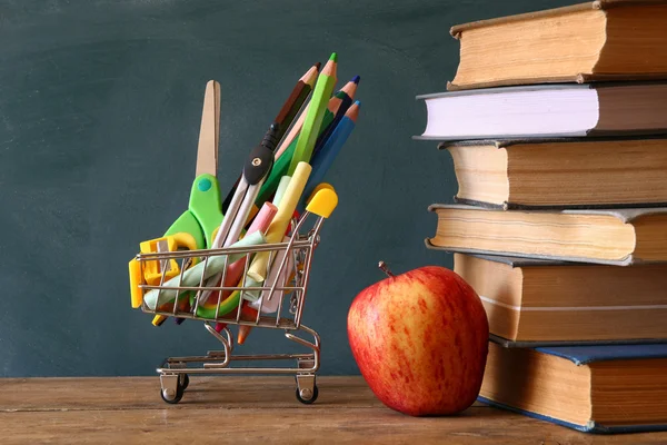 Carrinho de compras com material escolar, maçã e livros — Fotografia de Stock