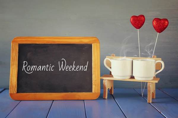 Coffee cups next to blackboard with text: ROMANTIC WEEKEND — Stock Photo, Image