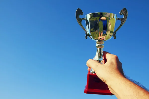 Mannen håller upp en trophy cup som en vinnare mot den blå himlen — Stockfoto