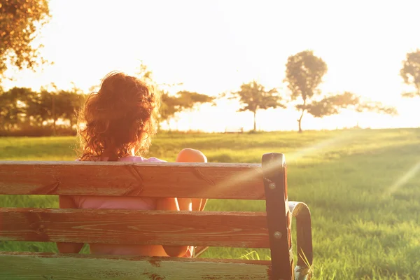 Πίσω όψη του παιδί που κάθεται στον πάγκο στο ηλιοβασίλεμα στο πάρκο — Φωτογραφία Αρχείου