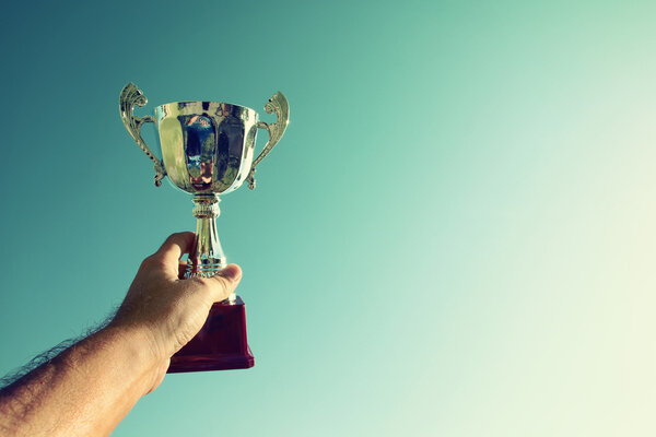 Man holding up a trophy cup as a winner against the blue sky