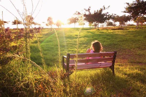 Visão traseira do garoto sentado no banco ao pôr do sol no parque — Fotografia de Stock