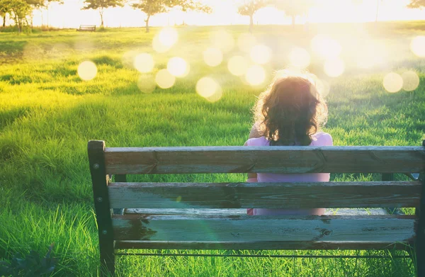 Πίσω όψη του παιδί που κάθεται στον πάγκο στο ηλιοβασίλεμα — Φωτογραφία Αρχείου