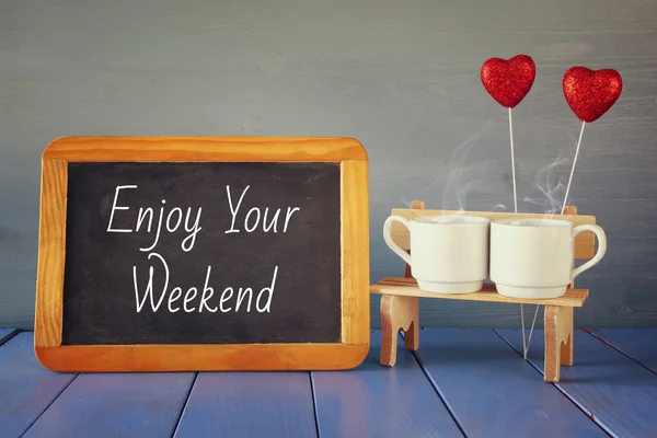 Tazas de café al lado de la pizarra con texto: DISFRUTA DE SU FIN DE SEMANA — Foto de Stock