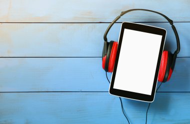 top view of tablet and headphones over wooden table clipart