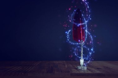 Eski tüylü mürekkep kalemi. Ahşap masa üzerinde mürekkep hokkası var. Arka planda siyah duvar var. Eski tarz ve filtrelenmiş. Tarih, eğitim, fantezi ve edebiyat konulu kavramsal fotoğraf