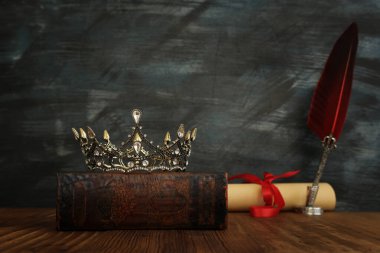 Eski kitapların üzerindeki güzel kraliçe / kral tacının ve ahşap masanın üzerindeki tüylü mürekkep kalemi. fantezi ortaçağ dönemi
