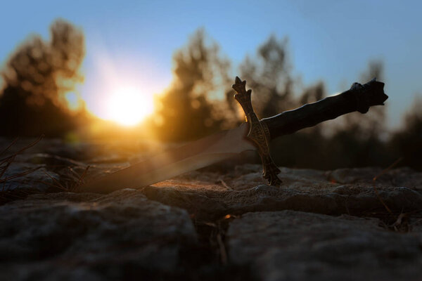 mysterious and magical photo of silver sword over stone in the England woods. Medieval period concept