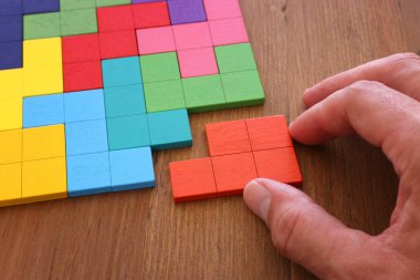 Bir adamın eli ahşap bir masanın üzerinde kare bir tangram yapbozu tutuyor.