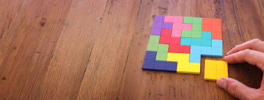 Bir adamın eli ahşap bir masanın üzerinde kare bir tangram yapbozu tutuyor.