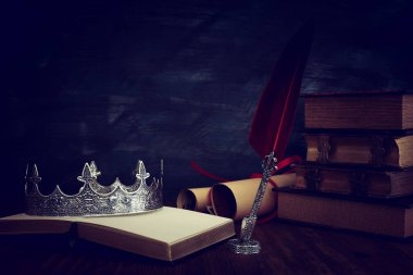 Güzel kraliçe / kral tacının gösterişsiz görüntüsü, eski kitaplar ve ahşap masanın üzerine tüy kalem. fantezi ortaçağ dönemi