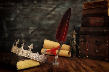 Güzel kraliçe / kral tacının gösterişsiz görüntüsü, eski kitaplar ve ahşap masanın üzerine tüy kalem. fantezi ortaçağ dönemi