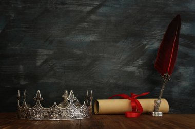 Güzel kraliçe / kral tacının loş görüntüsü ve ahşap masanın üzerine tüy kalem. fantezi ortaçağ dönemi