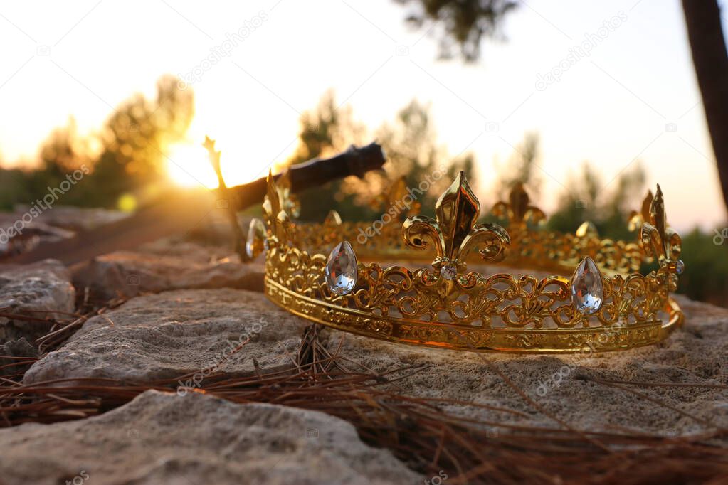 mysterious and magical photo of gold king crown and sword in the England woods over stone. Medieval period concept.