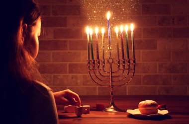 Low key image of jewish holiday Hanukkah background with girl looking at menorah (traditional candelabra) and burning candles clipart