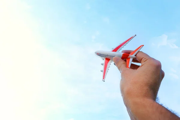 close up photo of man\'s hand holding toy airplane against blue sky with clouds. filtered image