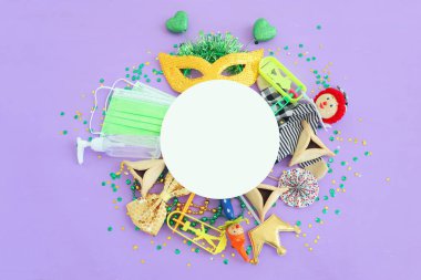 Purim kutlama konsepti (Musevi karnaval tatili) mor arka planda. Üst manzara, düz yatış. Coronavirus önleme konsepti, tıbbi maske ve dezenfektan jeli