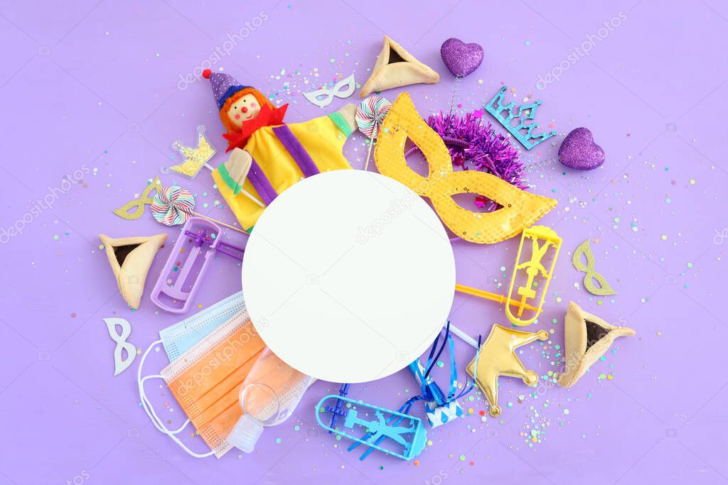 Purim celebration concept (jewish carnival holiday) over purple background. Top view, Flat lay. Coronavirus prevention concept, medical mask and sanitizer gel