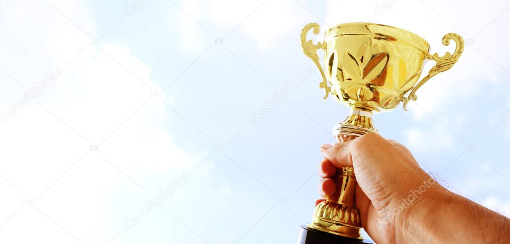 Man holding up a trophy cup as a winner against the blue sky. Award and victory concept