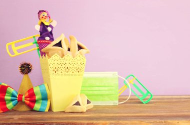 Ahşap masa ve mor arka plan üzerine Purim bayramı konsepti (Musevi karnavalı). Coronavirus önleme konsepti, tıbbi maske