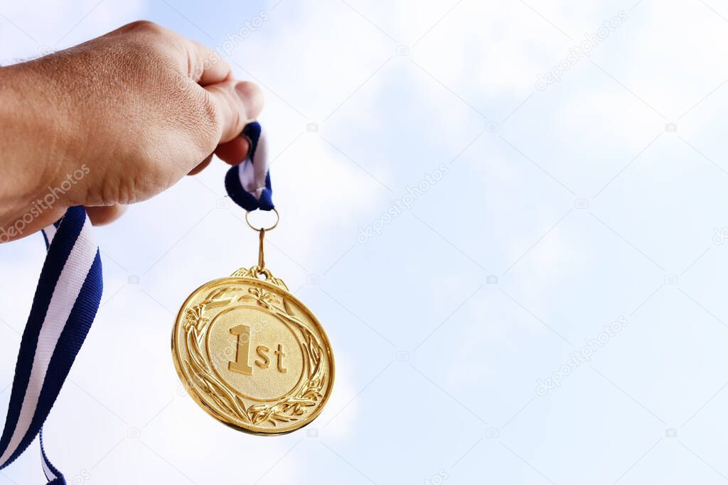 man hand raised, holding gold medal against sky. award and victory concept