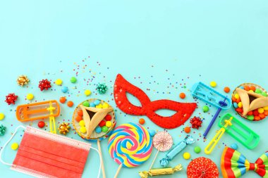 Purim bayramı konsepti (Yahudi karnavalı bayramı) mavi arka planda. Üst manzara, düz yatış. Coronavirus önleme konsepti, tıbbi maske