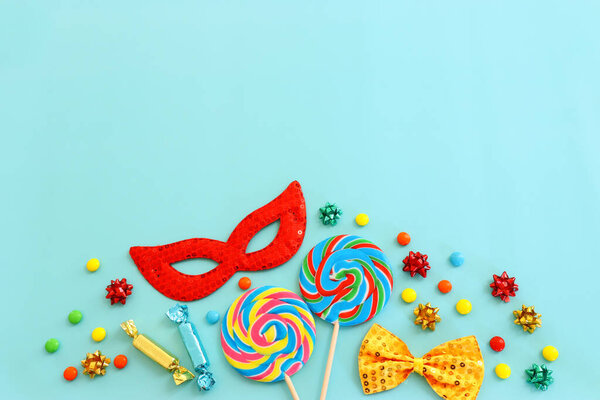 Праздничная красочная маска, леденцы и конфеты на синем фоне. Вид сверху, плоский