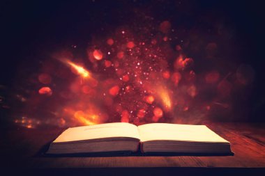 Tahta masanın üzerinde parıltılı kaplamalı açık antik kitabın sihirli görüntüsü.