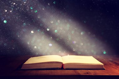 Tahta masanın üzerinde parıltılı kaplamalı açık antik kitabın sihirli görüntüsü.