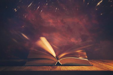 Tahta masanın üzerinde parıltılı kaplamalı açık antik kitabın sihirli görüntüsü.