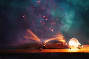 Tahta masanın üzerinde parıltılı kaplamalı açık antik kitabın sihirli görüntüsü.