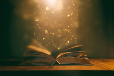 Tahta masanın üzerinde parıltılı kaplamalı açık antik kitabın sihirli görüntüsü.