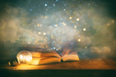 Tahta masanın üzerinde parıltılı kaplamalı açık antik kitabın sihirli görüntüsü.