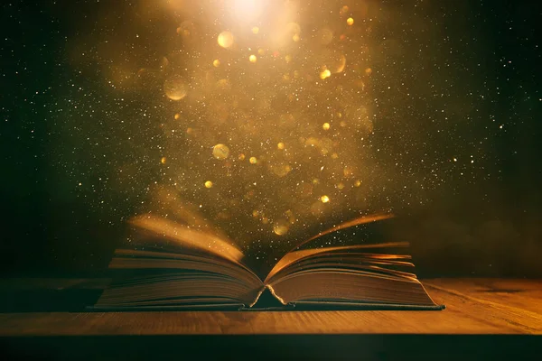 Tahta masanın üzerinde parıltılı kaplamalı açık antik kitabın sihirli görüntüsü.