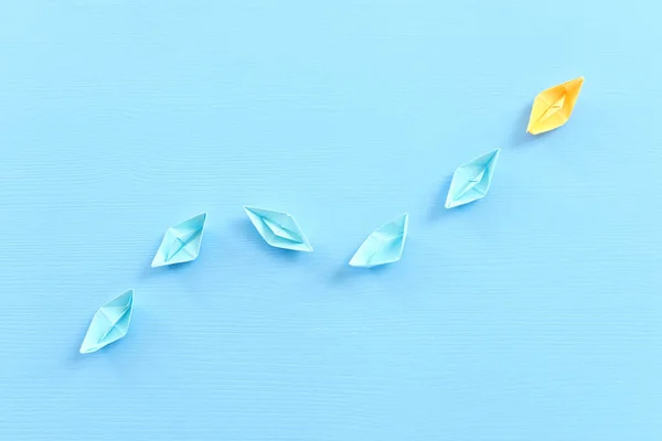 business. Leadership concept image with paper boats on blue wooden background. One leader guiding others.