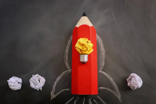 Education concept image. Creative idea and innovation. Crumpled paper as light bulb metaphor and rocket from pencil over blackboard