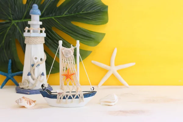 白い装飾の帆のボート 木製のテーブルと黄色の背景に貝殻と航海の概念 — ストック写真