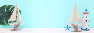 Beyaz dekoratif yelkenli tekne, ahşap masa üzerinde deniz kabukları ve mavi arka plan ile denizcilik kavramı