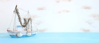 Beyaz dekoratif yelkenli tekne, ahşap masa üzerinde deniz kabukları ve beyaz arka plan ile denizcilik kavramı