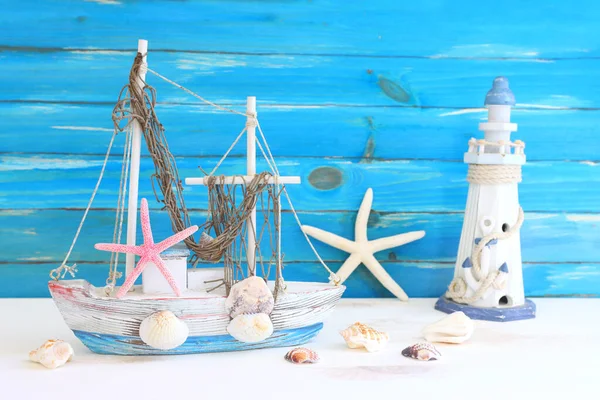 白い装飾の帆のボート 木製のテーブルと青の背景の上に貝殻と航海の概念 — ストック写真