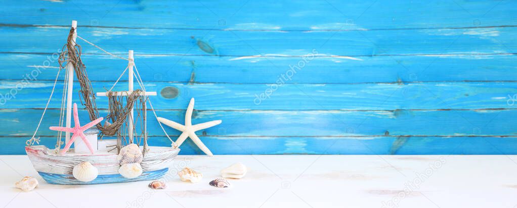 nautical concept with white decorative sail boat, seashells over wooden table and blue background