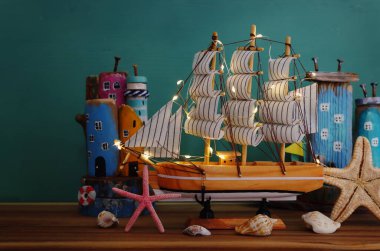 Deniz hayatı tarzı nesnelerle ilgili denizcilik kavramı. Işıklı tekne, dalgalı sahil evleri, ahşap masa üzerinde deniz kabukları ve deniz yıldızı gibi.